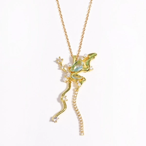 Détails macro du collier papillon doré avec gemme verte, perles et strass brillants