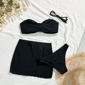 Flat lay of black three-piece bikini set with sheer mesh skirt and beach accessories