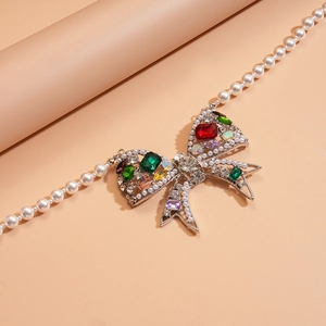 Close-up of a bow pendant with colorful gemstones and white pearls on a sleek necklace