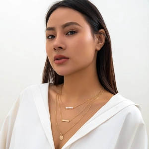 Close-up of layered gold necklace with pearls and geometric pendants on a model