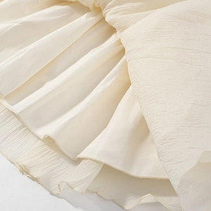 Macro shot of off-white dress fabric showing detailed 3D texture and soft pleats