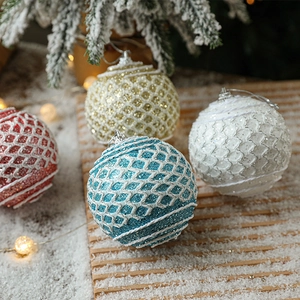 Close-up of glittery Christmas ball ornaments with scale textures on a snowy wooden tray