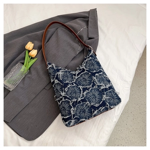 Blue denim tote bag with white floral embroidery and brown leather strap on white linen