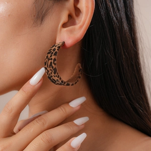 Close-up of a leopard print flocked C-shape hoop earring worn by a model in soft lighting