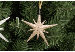 Close-up of a sparkling gold star Christmas ornament with glitter hanging on green branches