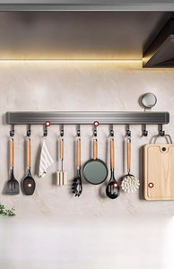 Detail of kitchen wall rack with hooks holding spatulas, pans and cutting board