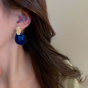 Macro view of blue teardrop acrylic earring with golden textured metal stud on model