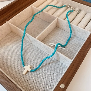 Detail of bohemian turquoise seed bead necklace with white stone cross pendant in a box