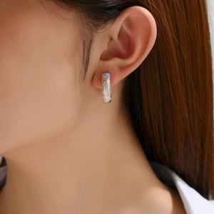 Detailed close-up of light blue enamel huggie hoop earrings with pink flower patterns