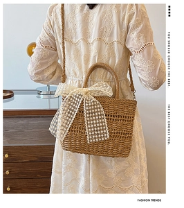 Detail of straw woven crossbody bag with large white lace bow shown on a white dress