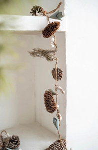 Detail of pine cones, white berries, and dried leaves on rustic jute rope decor