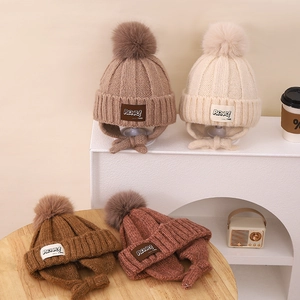 Detail of knit kids winter hats with ear flaps and pom-poms in multiple earth tones