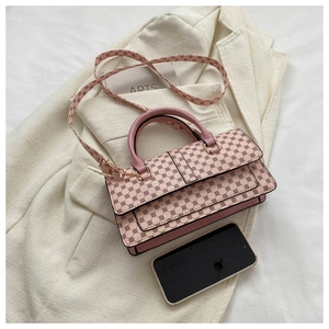 Detailed view of pink geometric patterned crossbody bag with gold hardware on white fabric
