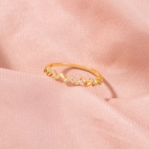 Macro detail of gold leaf ring with micro-set zircon and pearl on pink satin background