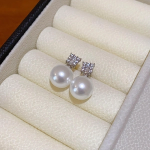 Close-up of pearl earrings with cubic zirconia inlay on a beige velvet jewelry box