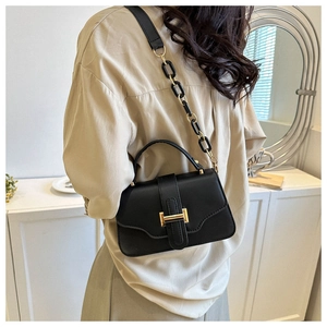 Detail of black faux leather handbag featuring a gold buckle and chain shoulder strap