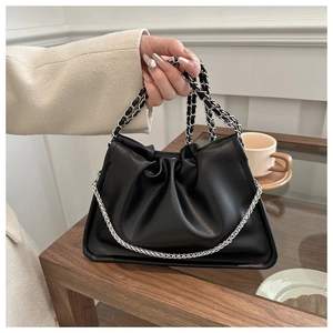Detail of black pleated cloud bag with silver woven chain strap held by a model in a cafe