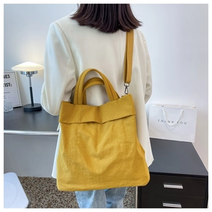 Detail view of mustard yellow nylon tote bag carried by a model in a minimalist setting