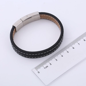 Gros plan sur un bracelet en cuir PU tressé noir avec fermoir en métal près d'une règle