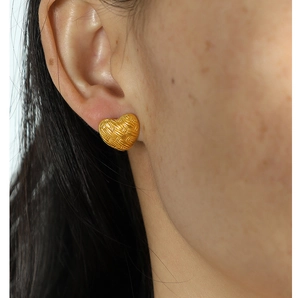 Detailed close-up of golden vintage heart stud earring with woven texture on model