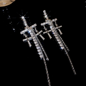 Detailed macro of silver cross tassel earrings with sparkling rhinestones on dark mirror