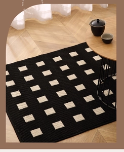 Detail of black woven doormat with white square patterns on light wood floor