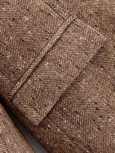 Vue macro du tissu en tweed à chevrons marron montrant les détails de couture du blazer