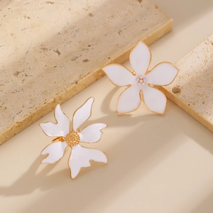 Détail de boucles d'oreilles fleurs blanches à bords dorés sur socle en pierre