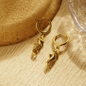 Detail of golden seahorse dangle earrings featuring a polished hoop and textured marine design