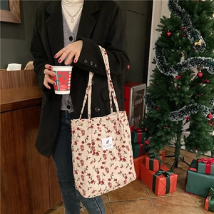 Detailed shot of floral corduroy tote bag showing red rose pattern and white woven label