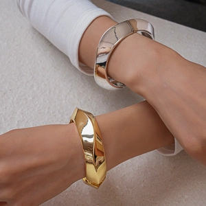 Close-up of chunky gold and silver oval geometric bangles on a model's wrist