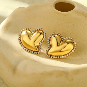 Boucles d'oreilles cœur dorées avec strass blancs sur fond beige de texture mate