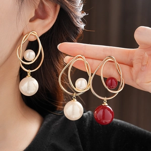 Close-up of irregular gold earrings with white and red pearl accents on a model