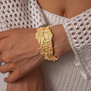 Detailed view of wide gold metal cuff bracelet with irregular crumpled lava texture
