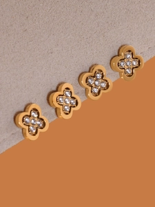 Detail of four golden clover charms with pavé set crystals on a stylish bicolor background