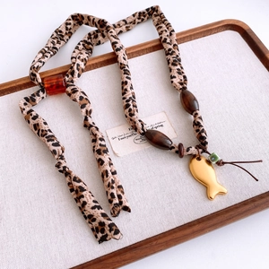 Macro detail of leopard fabric cord necklace with golden fish charm and wood beads