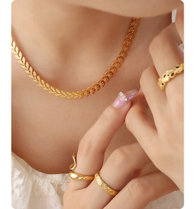 Detail of 18K gold wheat leaf necklace and textured rings on a model in lace
