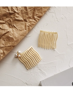 Detail of golden metal hair combs with pearl clusters on a clean white textured surface