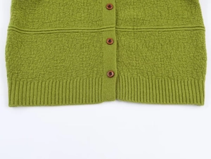 Detail of green textured boucle knit fabric with brown buttons and ribbed hem finish