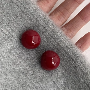 Deep red cherry spherical stud earrings with glossy finish on grey knitted fabric