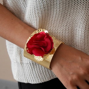 Detailed macro view of a large red fabric rose on a textured gold metallic cuff bracelet