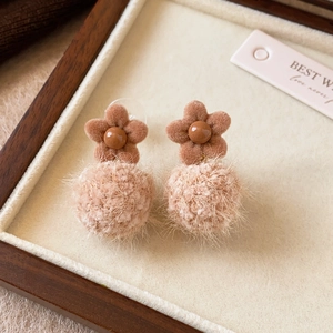 Detail of flocking flower earrings with soft plush pom poms in brown and beige tones