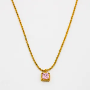 Détail d'un collier chaîne torsadée dorée avec pendentif zircon rose carré sur fond blanc
