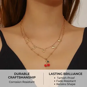 Close-up of double-layer gold chain necklace featuring red cherry pendant on a model