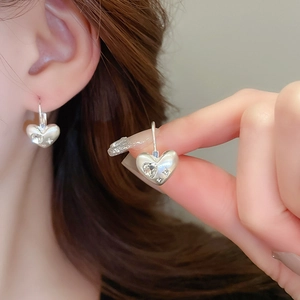 Detailed close-up of silver heart-shaped earrings with inlaid clear zircons on ear lobe