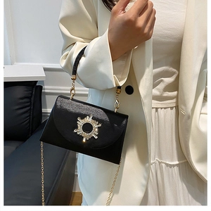 Detail of glossy black handbag with sunflower crystal decor and beaded handle on a model