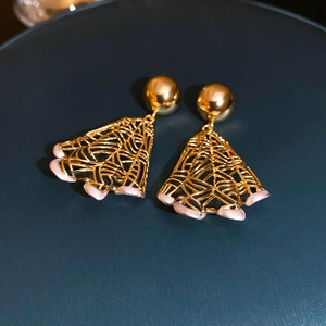 Detail shot of golden fan-shaped hollow earrings with pink shell accents on blue display