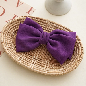 Detailed close-up of dark purple textured fabric bow hair clip in a woven basket
