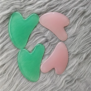 Detailed view of four pink and green facial gua sha scraper tools on a soft plush background