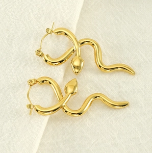 Detail of snake-shaped 18k gold-plated titanium earrings on textured fabric background